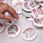 (शनिबार, अक्टोबर १७, २०२६ मा सिएटलमा आयोजित "वाशिङ्टन राज्यमा घृणा निषेध" र्‍यालीका क्रममा एक व्यक्तिले एउटा 'बटन' (ब्याज) उठाउँदै। उक्त र्‍याली नोभेम्बरको मतपत्रमा समावेश विभिन्न प्रस्तावहरू (initiatives) को विरोधमा थियो; तीमध्ये 'वाशिङ्टन स्टेट इनिसिएटिभ ६३८' पनि एक हो, जसले ट्रान्सजेन्डर केटीहरूलाई छात्रा खेलकुद प्रतियोगिताहरूमा भाग लिनबाट निषेध गर्नेछ। एपी तस्बिर: लिन्डसे वासन)